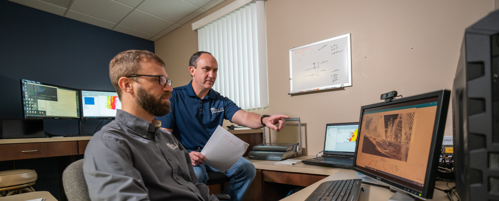 two men talking at a computer in an office