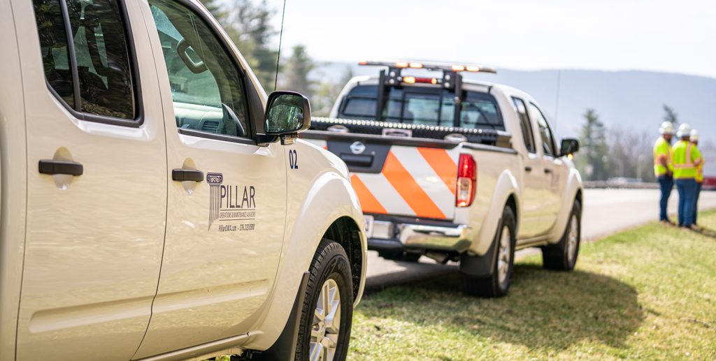 PILLAR Trucks parked on side of the road inspecting a landslide